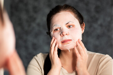 Evening skincare routine. Female applying nourishing face mask. Late night face care. Reflection in...