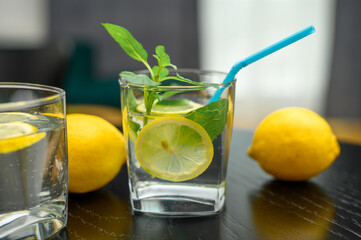 Water with lemon in a glass, a drink with a slice of lemon and a straw