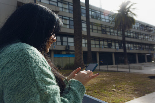 Rear view of unrecognizable woman using phone outside university