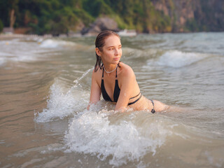 Young woman enjoying serene evening at sea in Krabi, Thailand during sunset. Calm waves, golden light, and peaceful atmosphere highlight tropical beauty and connection with nature.