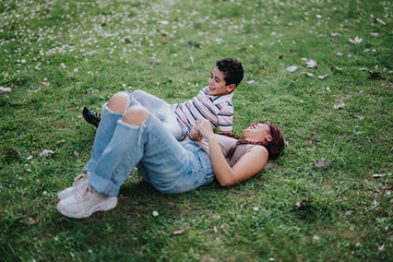 A joyful scene of a mother and her child enjoying quality time outdoors while lying on a grassy park field, smiling and sharing a laugh. Captures warmth, family bonding, and happiness in nature.