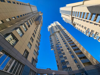 The sky is blue and the buildings residential complex are tall. The buildings are brown and have many windows. The sky is clear and the sun is shining