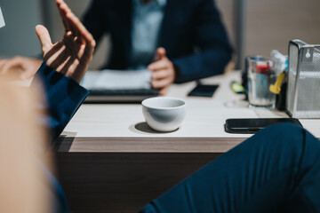 Two business people collaborate at an office desk with coffee, discussing work concepts and tasks.