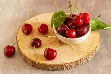 A white ceramic bowl filled with glossy, deep red cherries, placed on a round wooden cutting...