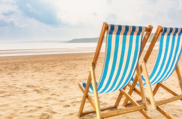 Wooden deck chairs on a sandy beach with a headland in the distance.