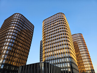 Three tall buildings with windows and a blue sky in the background. The buildings are made of glass...