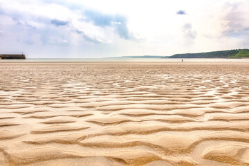 A sandy beach where a receding tide has left ripples of sand and puddles of water.