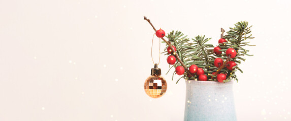 Banner with bouquet of nobilis fir and winterberry branches in a vase with golden Christmas bauble in front of beige background.