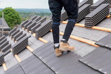 Roofer carefully places slate roofing tiles on a structure's roof ensuring proper alignment and...