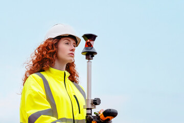 Young female surveyor operates a total station at a construction site while wearing safety hi-viz...