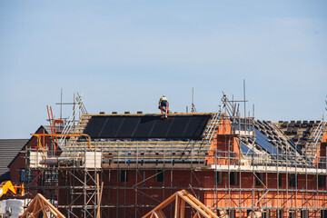 Fototapeta premium Builder stands on top of the sloped roof while fixing new solar panels