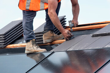 Construction worker roofers installing roofing tiles on residential building