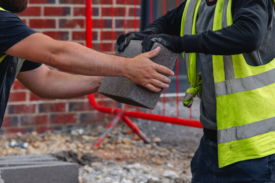 Example of manual handling as bricklayers moving concrete footing blocks by hand on building site