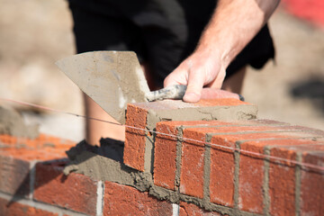 Close-up of Skilled worker laying bricks with trowel on construction site