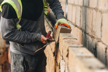 Bricklayer constructing stone wall using stone blocks, cement mortar mix and trowel