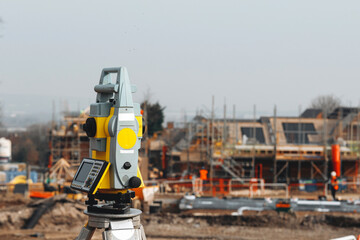 Close-up of Land surveyors equipment theodolite or total positioning station set on tripod on construction site by land surveyor for measurements with construction activities in background