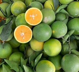 This image captures a vibrant display of fresh, mostly green oranges, some still adorned with their...