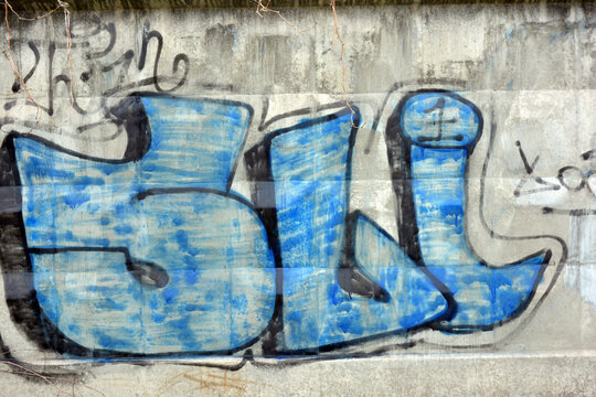 Graffiti word 5LI, drawn by a lapdog in sky blue with black letters with an big shape. Graphic design made in chaotic way when a paint can be washed on a concrete fence near the railway tracks.