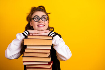 Smiling teenage girl with glasses leaning on a stack of book against a vibrant yellow background