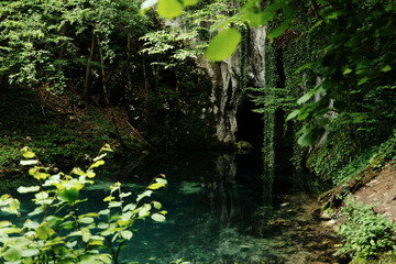 Cave entrance surrounded by lush green forest and turquoise water at Krupajsko vrelo, Serbia country in spring season.