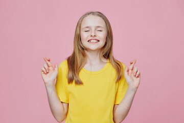Cheerful girl with crossed fingers, wearing a bright yellow shirt, expresses hope and excitement...