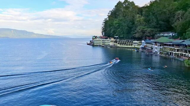 Lake Toba's natural landscape is filled with tropical trees. Activity of fishing boats, speed boats on the largest volcanic lake in Indonesia.