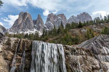 Close view of waterfall with the Geisler Peaks in the Dolomites in the background, surrounded by...