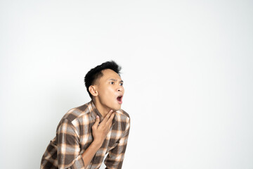 Asian young man dressed casually in a checked shirt touching his throat while looking concerned.