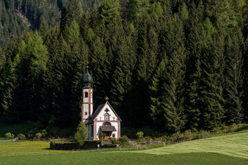 Church of St. John in Ranui in Val di Funes, Italy, with alpine meadow and Geisler Peaks in the background.