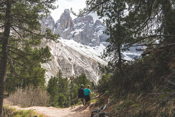 Couple sitting on bench in alpine forest enjoying snowy Dolomites mountain view in Italy.