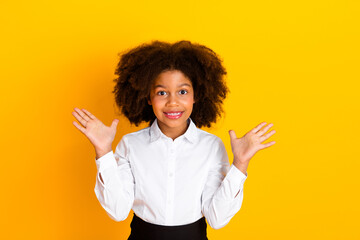 Portrait of a cheerful young girl in a white shirt expressing surprise against a bright yellow...