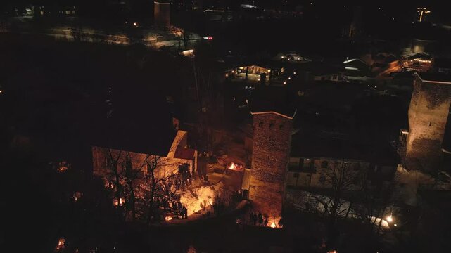 Aerial night view Lamproba festival with villagers gathered around symbolic bonfires near church and medieval tower in Svaneti.Concept welcoming arrival of spring, invite the blessings of the gods
