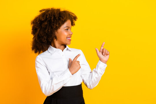 Smiling schoolgirl in a white shirt pointing with both hands against a yellow background showcasing a bright gesture - Powered by Adobe