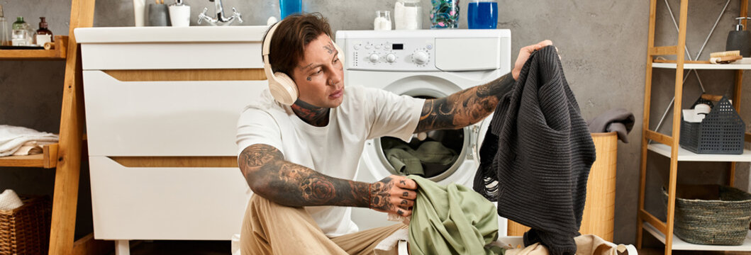 Handsome tattooed man enjoys a cozy time at home while doing laundry and listening to music - Powered by Adobe