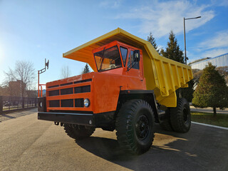 A yellow and orange dump truck is parked on a street. The truck is parked in front of a building