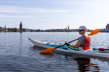 Woman kayaking on Riddarfj&auml;rden in Stockholm, with City Hall (Stadshuset) and historic spires of the old town in the distance.