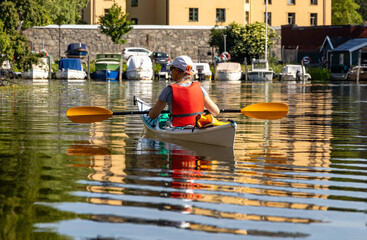 Woman paddling a kayak through calm urban waters with moored boats and historic stone walls in the...