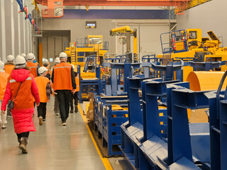 A group of people are walking through a factory with blue and yellow machinery electric motor and...