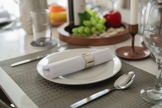 Elegant dining table setting with refined tableware, neatly arranged napkin, wine bottle, fresh fruits, and decorative elements for special occasions