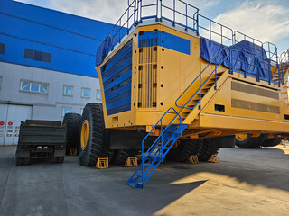 A large yellow and blue truck and small normal size together. The truck is parked in a lot next to...