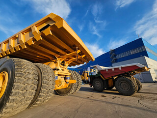 A large yellow truck is parked next to a blue building. The truck is surrounded by two other...