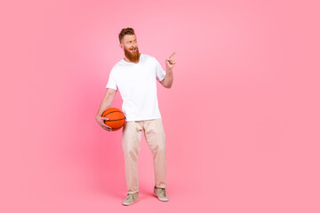Casual bearded man holding basketball against pink background, gesturing with confidence and style,...
