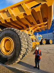 A man in a safety vest stands next to a large yellow truck. The man is looking at a clipboard