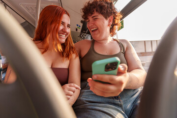 Two women riding public transit, smiling together while scrolling smartphones, sharing casual camaraderie during urban commute