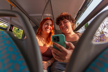 Two young women smiling and using a smartphone while sitting on a bus, enjoying their journey together