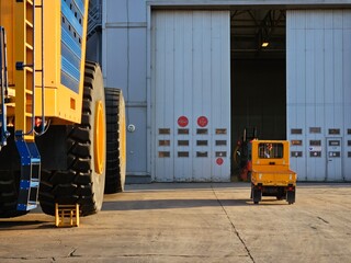 A large yellow truck is parked next to a smaller yellow truck. The smaller truck is being driven by...