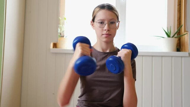 14 years old teenager customized workout, a mix of strength training, flexibility exercises, and cardio at home. Authentic shot. Teen girl exercises with dumbbells. Holistic Health, Mental WellBeing