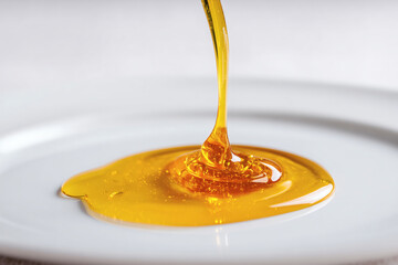 Golden syrup cascading onto a white surface, creating a shimmering puddle, perfect for culinary use.