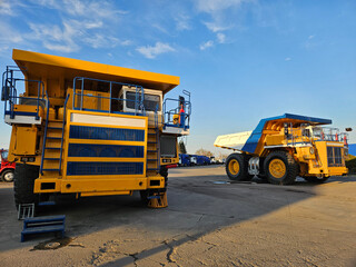 Two large yellow and blue trucks are parked in a lot.