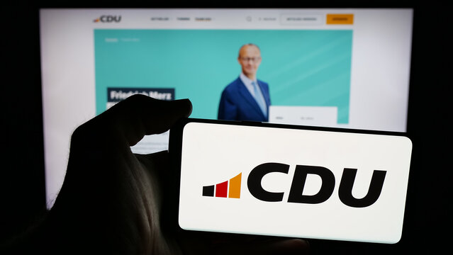 Stuttgart, Germany - 06-25-2025: Person holding mobile phone with logo of party Christlich Demokratische Union (CDU) on screen in front of web page. Focus on phone display.